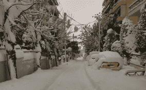 Χιονισμένος δρόμος άδειος με αυτοκίνητα σκεπασμένα με χιόνι και γερμένα δέντρα
