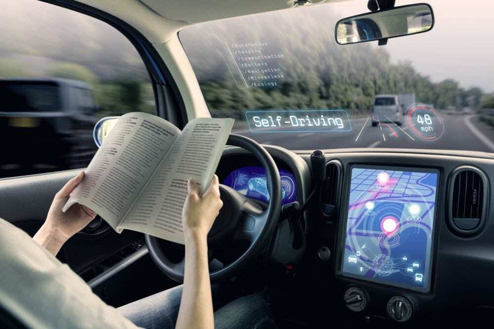 Εικόνα από το εσωτερικό αυτοκινήτου, γυναίκα οδηγός κρατά βιβλίο ενώ το αυτοκίνητο κινείται μόνο του