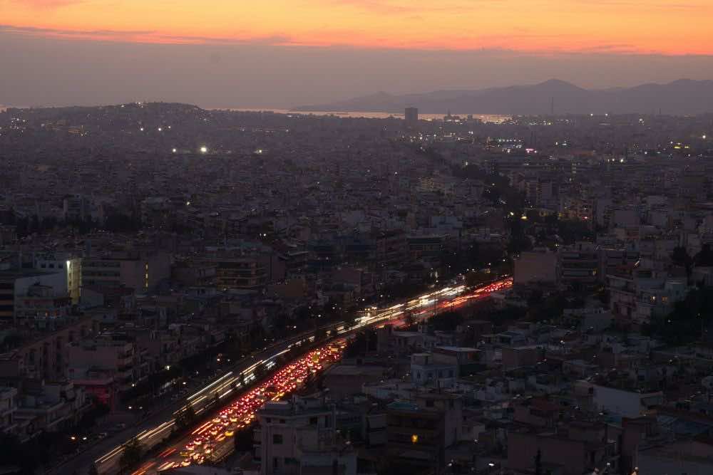 Η Αθήνα από ψηλά το σούρουπο, φώτα αυτοκινήτων φωτίζουν τον δρόμο 