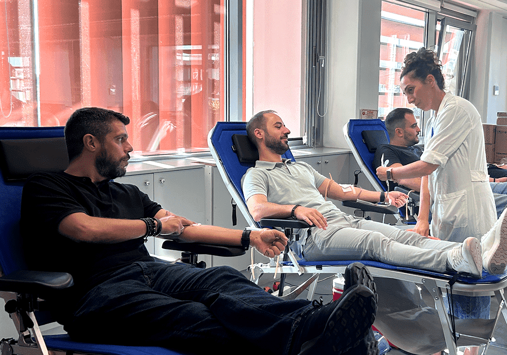 τρεις άνδρες ξαπλωμένοι σε κρεβάτια αιμοδοσίας, νοσηλεύτρια ελέγχει τον έναν