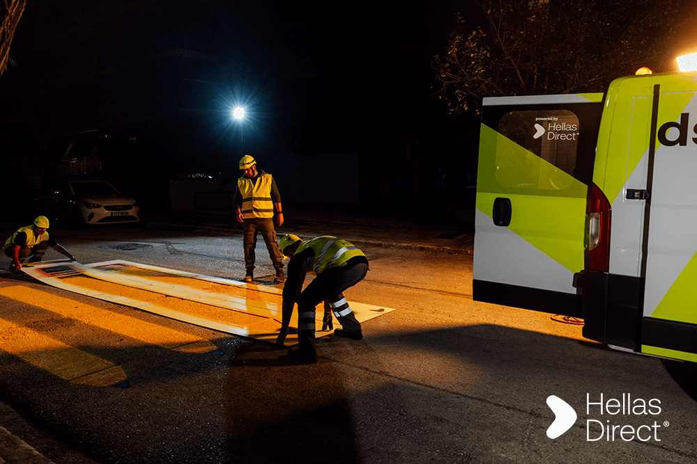 Νύχτα στον δρόμο, το συνεργείο βάφει διάβαση πεζών με κίτρινα μολύβια, δεξιά το βαν του Safe Roads project