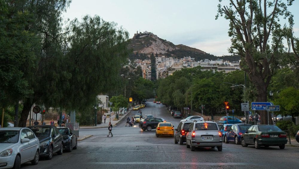 εικόνα Αθήνας, αυτοκίνητα στον δρόμο, στο φόντο δέντρα, σπίτια και ο Λυκαβηττός