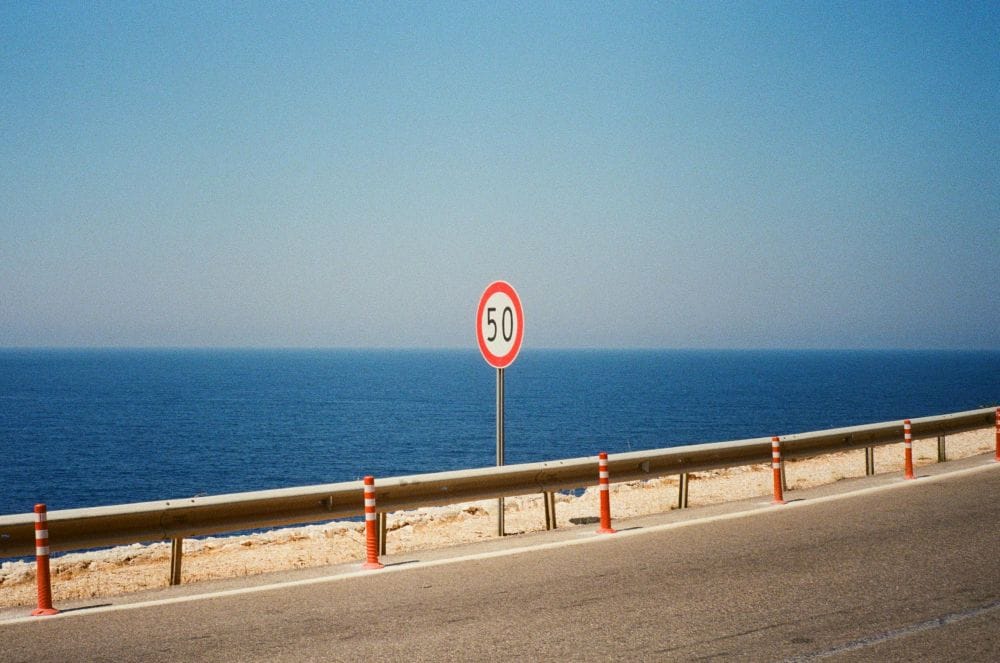 πινακίδα που δείχνει 50 τοποθετημένη δίπλα στις μπάρες δρόμου με φόντο θάλασσα