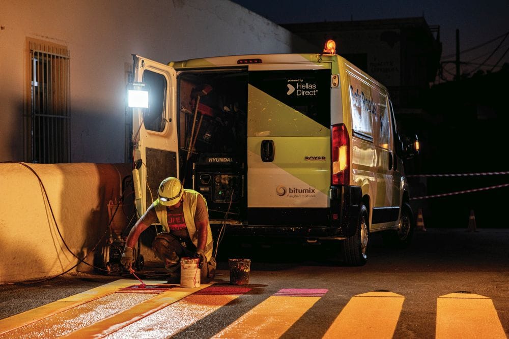 νύχτα στον δρόμο, μέλος του συνεργείου του Safe Roads βάφει διάβαση με κίτρινα μολύβια, στο φόντο το βαν με ανοιχτή την πίσω πόρτα
