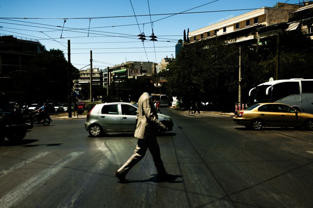 Κίνηση στο κέντρο της Αθήνας, πεζός διασχίζει μεγάλο δρόμο και πίσω του αυτοκίνητα μηχανές πούλμαν