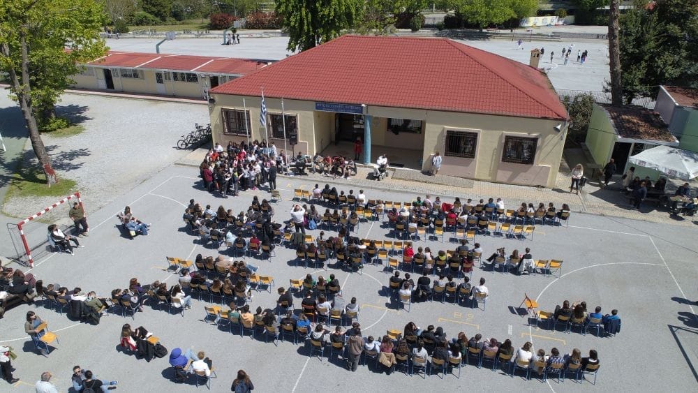 φωτογραφία από ψηλά, μαθητές καθισμένοι σε προαύλιο σχολείου, ακούν τον Δημήτρη Αντωνίου