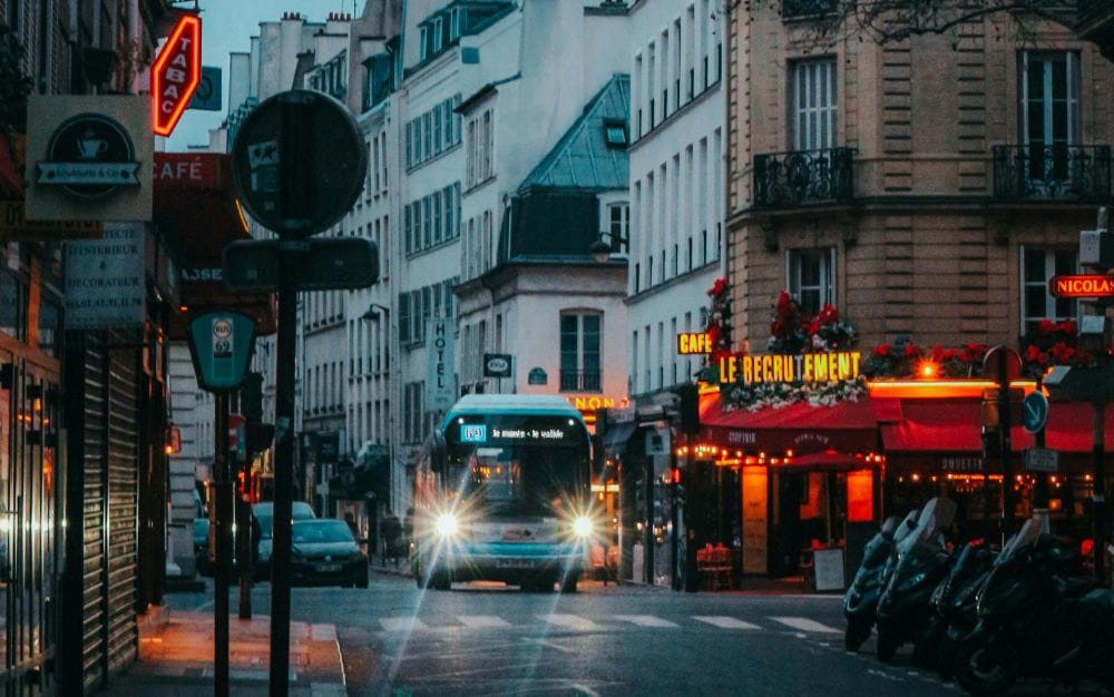 δρόμος στο Παρίσι, λεωφορείο ανφας με τα φωτα αναμμένα, στο πλάι κτίρια και μπιστρό με φωτεινή πινακίδα