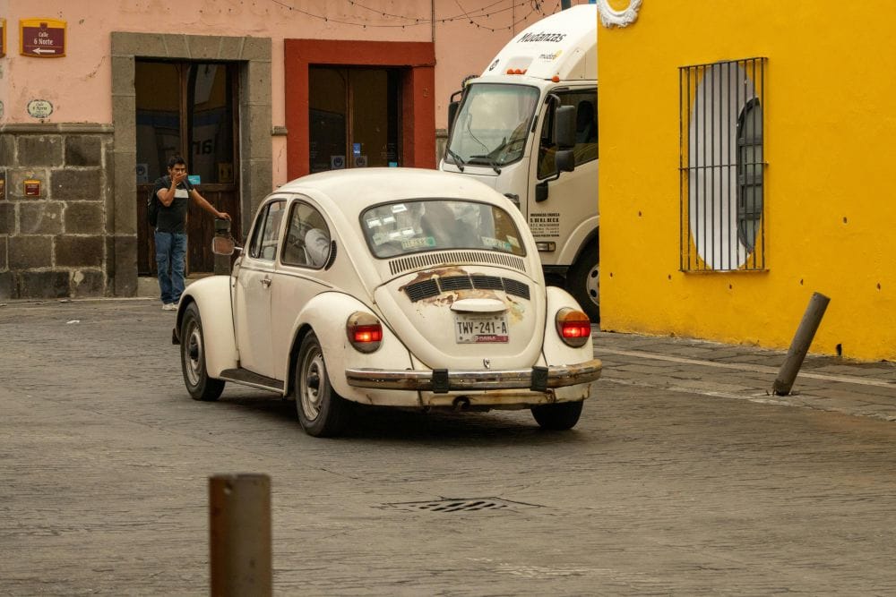 δρόμος στην λατινική Αμερική, λευκός παλιός Σκαραβαίος εν κινήσει από πίσω, στο φόντο πολύχρωμα κτίρια