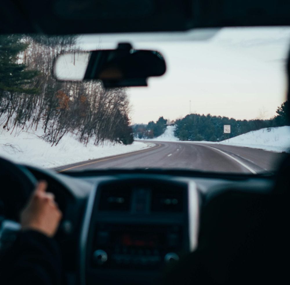 εικόνα χιονισμένου δρόμου μέσα από αυτοκίνητι, βλέπουμε χέρι στο τιμόνι και την καμπίνα του του οδηγού