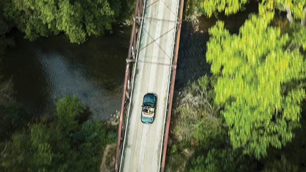 πράσινο Mazda MX-5 Miata από ψηλά ενώ κινείται σε γεφυρα πάνω από ποτάμι