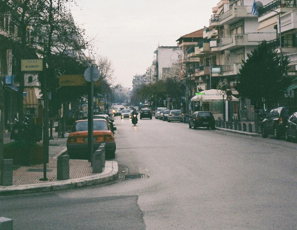 εικόνα πόλης, αυοτκίνητα παρκαρισμένα και σε κίνηση, δεξιά κι αριστερά πολυκατοικίες 