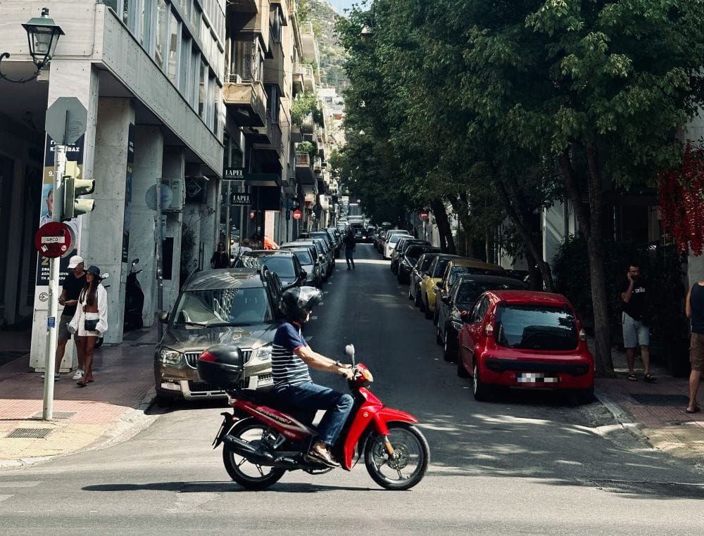 δρόμος πόλης μέρας για το θέμα πινακίδες κυκλοφορίας. Παρκαρισμένα αυτοκίνητα, μηχανάκι και πεζοί σε κίνηση σε ανηφορικό δρόμο. 