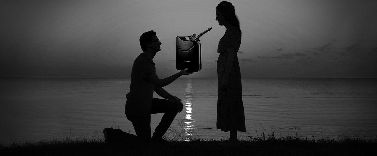 Ασπρόμαυρη εικόνα, άνδρας γονατίζει σε γυναίκα σαν πρόταση γάμου, κρατάει αντί για δαχτυλίδι μπιτόνι με βενζίνη