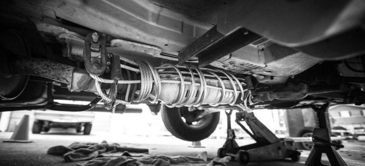 ασπρόμαυρη εικόνα, κάτω μέρος αυτοκινήτου σηκωμένου με γρύλους, καταλύτης δεμένος με συρματόσχοινο