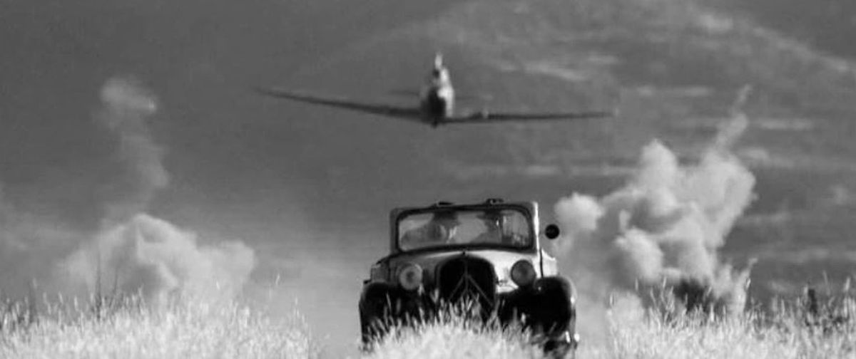 ασπρόμαυρο screenshot από ταινία Ιντιάνα Τζόουνς, αυτοκίνητο αντίκα και πίσω του πλησιάζει αεροπλάνο