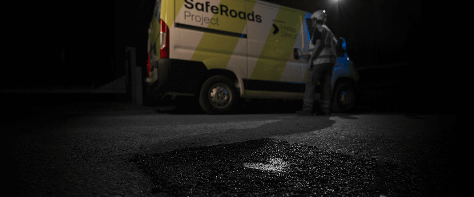 νύχτα στον δρόμο, μροστά λακκούβα φρεσκοφτιαγμένη με άσφαλτο, στο φόντο το βαν του Safe Roads