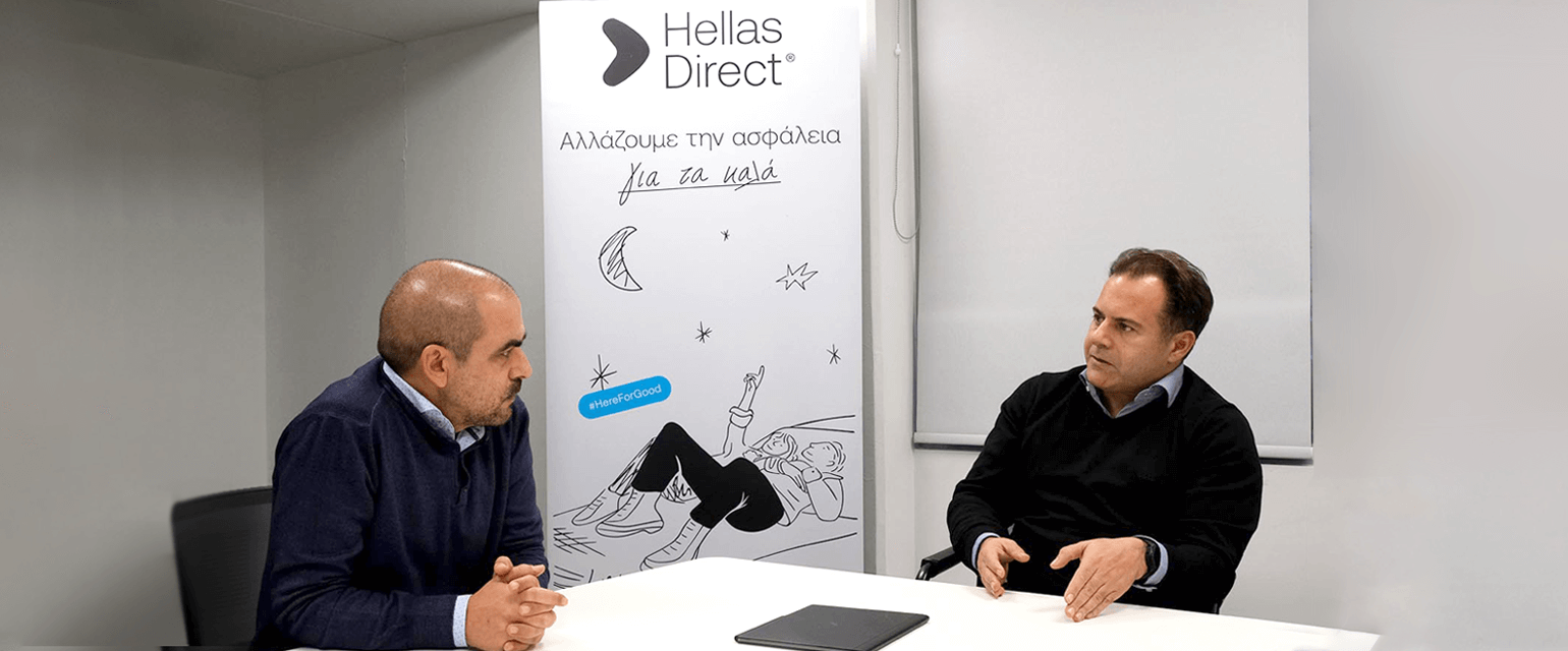 δύο άνδρες κάθονται και συνομιλούν, στη μέση banner με το μήνυμα Hellas Direct Αλλάζουμε την ασφάλεια για τα καλά 