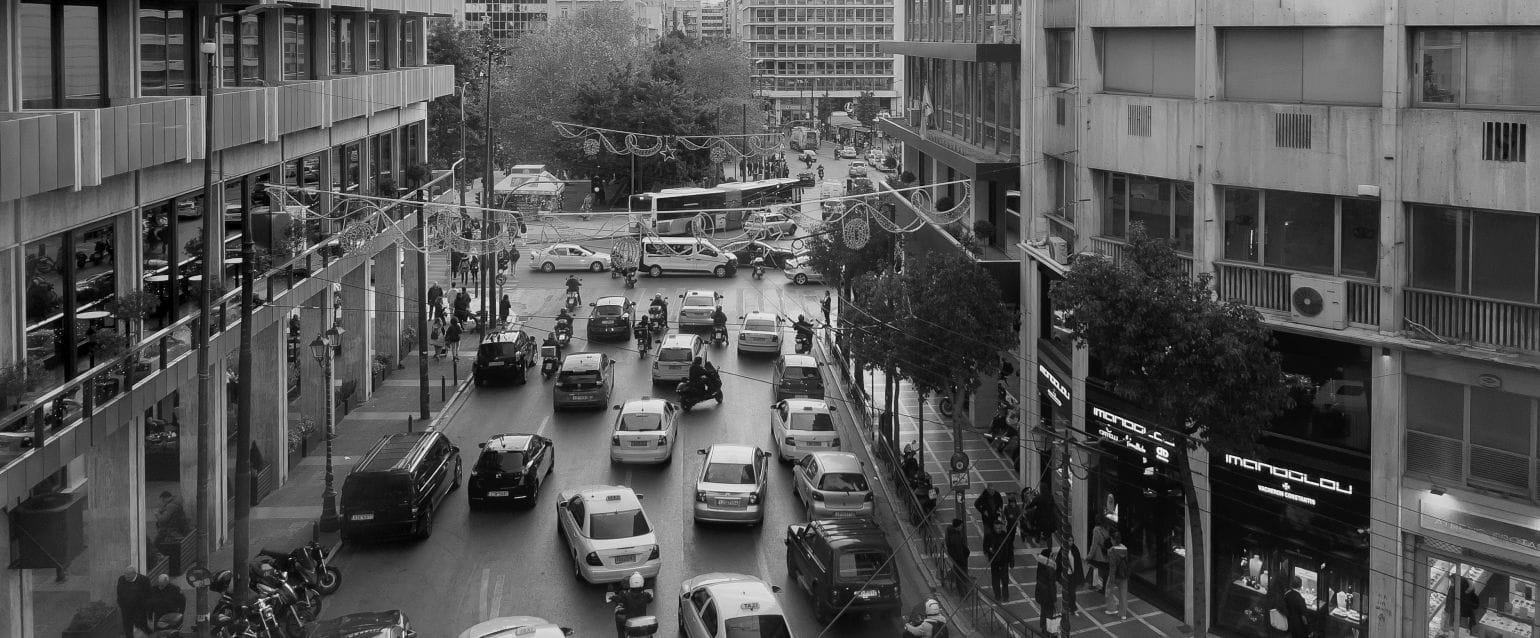 ασπρόμαυρη εικόνα, δρόμος της Αθήνας γεμάτος αυκίνητα, δεξιά αριστερά ψηλά κτίρια