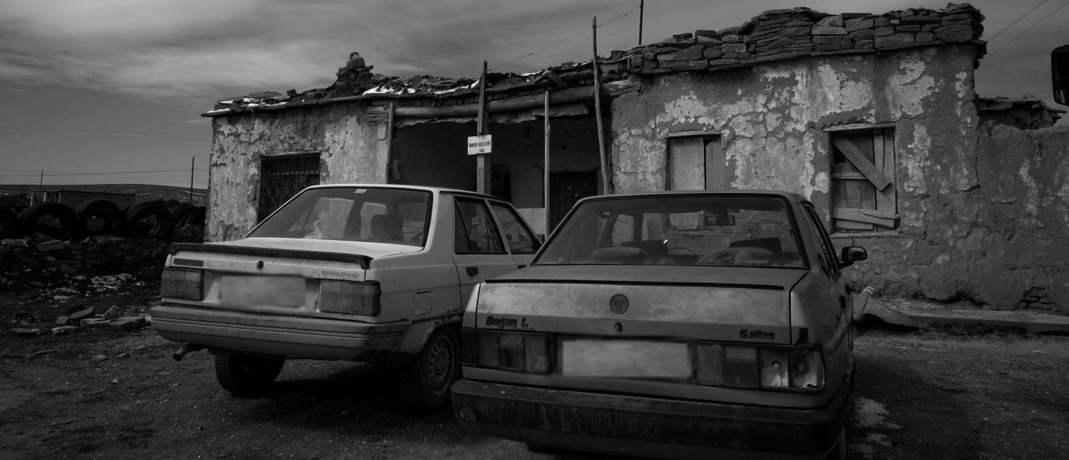 ασπρόμαυρη εικόνα, παλιά αυτοκίνητα παρκαρισμένα δίπλα δίπλα έξω από ερειπωμένο σπίτι