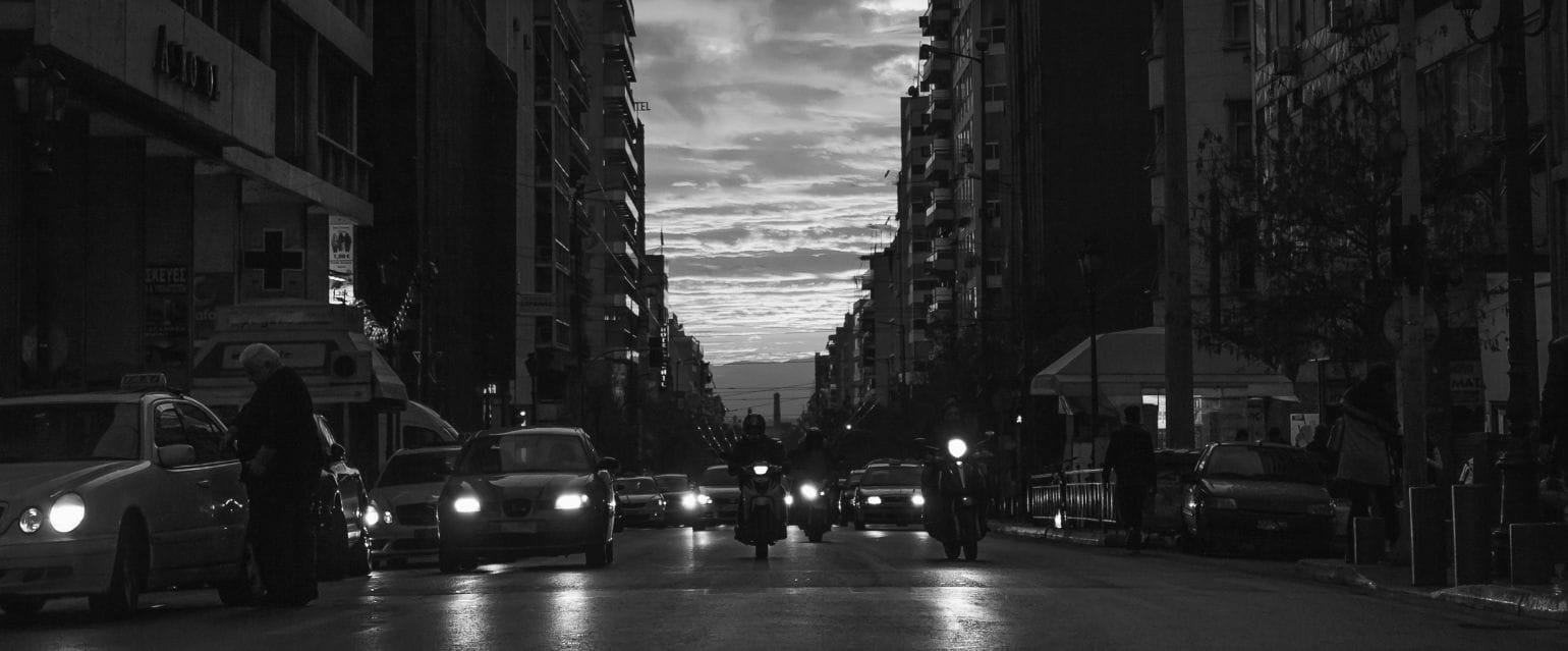 ασπρόμαυρη εικόνα, δρόμος πόλης για το θέμα πινακίδες κυκλοφορίας στην Ελλάδα - αλλαγές. Αυτοκίνητα και μηχανές εν κινήσει, στο φόντο σύννεφα