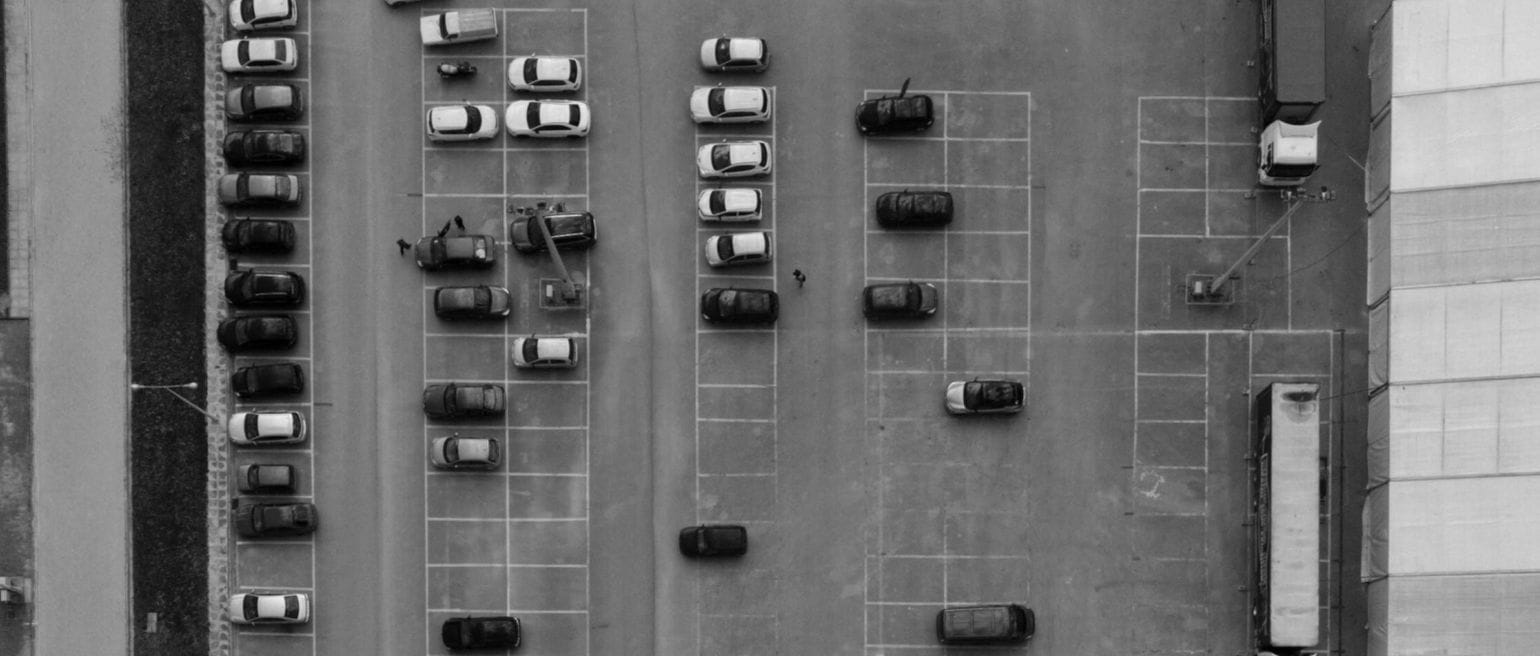 ασπρόμαυρη εικόνα για το θέμα: τεκμήρια αυτοκινήτων 2026. Πάρκινγκ αυτοκινήτων από ψηλά, σειρές με παράλληλα παρκαρισμένα αυτοκίνητα και κενές θέσεις