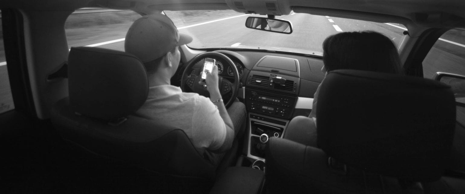 κινητό στην οδήγηση, καμπίνα αυτοκινήτου με δύο άτομα, ο οδηγός κρατάει στο χέρι κινητό ενώ οδηγεί