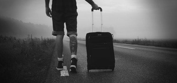 ασπρόμαυρη εικόνα, άνδρας περπατάει σε άδειο δρόμο σέρνοντας βαλίτσα με ροδάκια