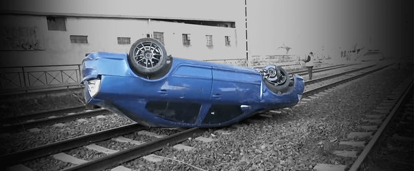 μπλε αυτοκίνητο αναπποδογυρισμένο πάνω σε ράγες, εικόνα από το πλάι